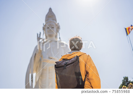Male tourist on the background of Majestic view of the Lady Buddha statue the Bodhisattva of Mercy, Vietnam. White Ladybuddha statue on blue sky background 75855988