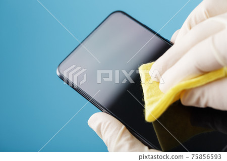 Cleaning a smartphone with a sterile yellow napkin in rubber gloves on a blue background. 75856593