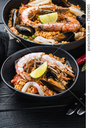Typical spanish seafood paella in traditional pan and black bowl on black wooden background Typical spanish seafood paella in traditional pan and black bowl on black wooden background 75856905
