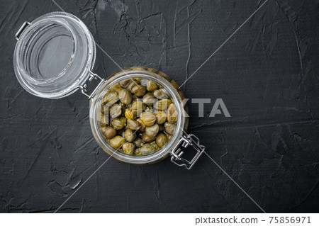 Baby capers in glass jar, on black background, top view with copy space for text Baby capers in glass jar, on black background, top view with copy space for text 75856971