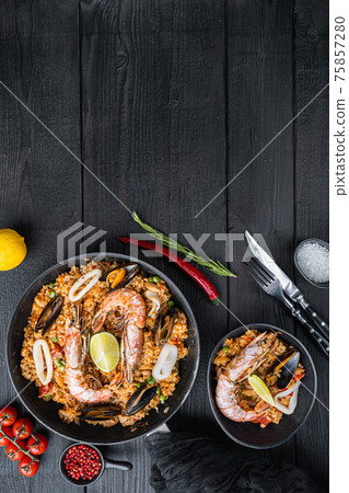 Typical spanish seafood paella in traditional pan and black bowl on black wooden background, flat lay with copy space Typical spanish seafood paella in traditional pan and black bowl on black wooden background, flat lay with copy space 75857280