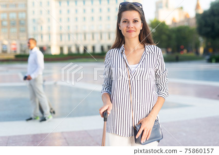 Young woman walking with baggage through city 75860157