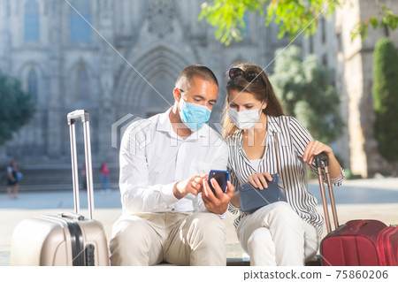 Couple of travelers in face masks reading about sights in smartphone Couple of travelers in face masks reading about sights in smartphone 75860206