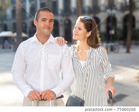Woman and man travelers walking with baggage through city Woman and man travelers walking with baggage through city 75860208