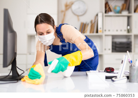 Woman in protective mask wipes dust from table in office 75860353