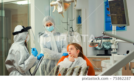 Dentist doctor in ppe suit taking notes on clipboard about little patient Dentist doctor in ppe suit taking notes on clipboard about little patient 75862287