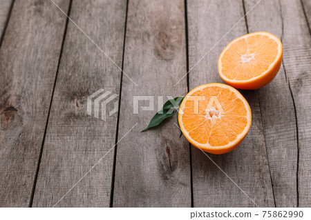 Halves of orange fruit on gray wooden background. Orange pulp and green leaves Halves of orange fruit on gray wooden background. Orange pulp and green leaves 75862990