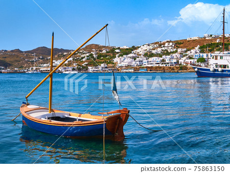 Beautiful summer day in typical Greek island. Fishing boats, whitewashed house. Small blue boat in foreground. Mykonos, Cyclades, Greece. Beautiful summer day in typical Greek island. Fishing boats, whitewashed house. Small blue boat in foreground. Mykonos, Cyclades, Greece. 75863150