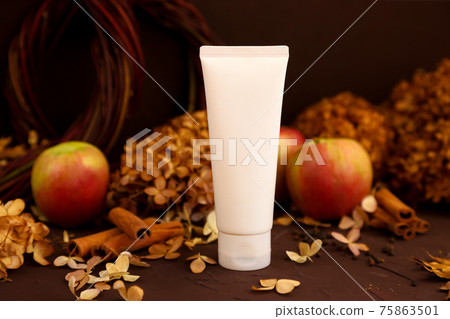 White squeeze cosmetic tube, autumn leaves, cinnamon, apples and dry hydrangea flowers on dark brown background, top view. White unbranded lotion, balsam, hand creme, toothpaste mockup. 75863501