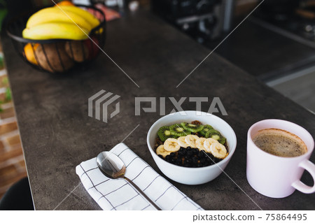 Pink coffee cup, bowl with chopped fruits and blueberries, spoon in kitchen Pink coffee cup, bowl with chopped fruits and blueberries, spoon in kitchen 75864495