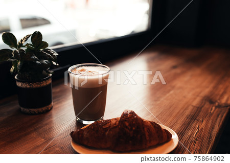 Cup of coffee, croissant at table near the window in cafe. Blurred background 75864902