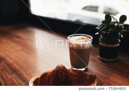 Cup of coffee, croissant at table near the window in cafe. Blurred background 75864903