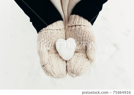 Snow heart snowball in girl gloved hands. Blurred background 75864916