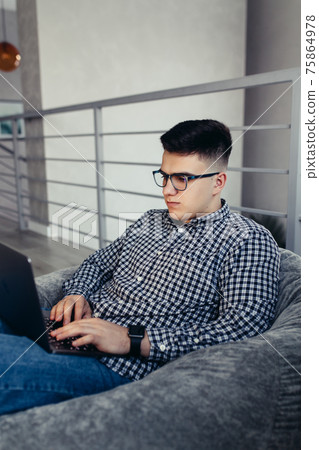 Man using laptop, wearing glasses, cushioned furniture. Blurred background 75864978