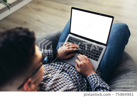Man using laptop, wearing glasses, cushioned furniture. Blurred background Man using laptop, wearing glasses, cushioned furniture. Blurred background 75864981