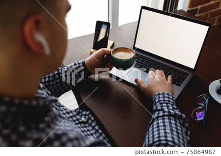 Man working at laptop with cup of coffee, headphones at home. Blurred background 75864987