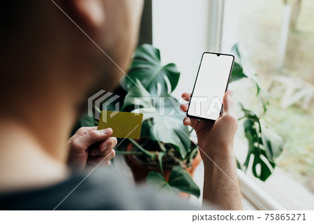 Man holds smartphone with white screen and bank card Man holds smartphone with white screen and bank card 75865271