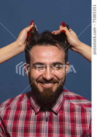 Female hands rumple young bearded handsome man on blue background Female hands rumple young bearded handsome man on blue background 75865351