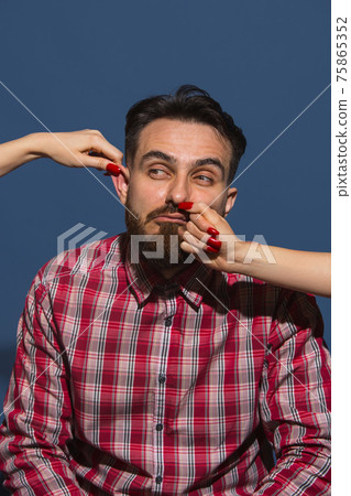 Female hands rumple young bearded handsome man on blue background Female hands rumple young bearded handsome man on blue background 75865352