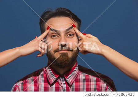 Female hands opening eyes of young bearded handsome man on blue background 75865423