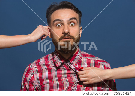 Female hands rumple young bearded handsome man on blue background Female hands rumple young bearded handsome man on blue background 75865424
