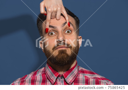 Female hand opening eyes of young bearded handsome man on blue background Female hand opening eyes of young bearded handsome man on blue background 75865425