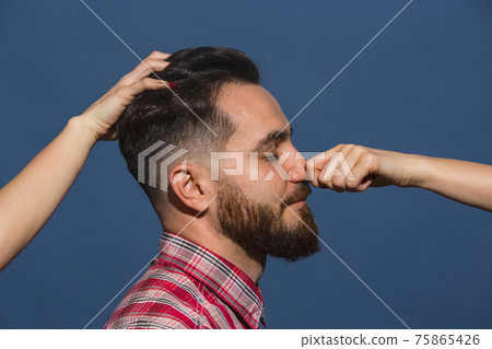 Female hands making different emotions of young bearded man on blue background Female hands making different emotions of young bearded man on blue background 75865426