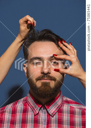 Female hands opening eye of young bearded handsome man on blue background Female hands opening eye of young bearded handsome man on blue background 75865441