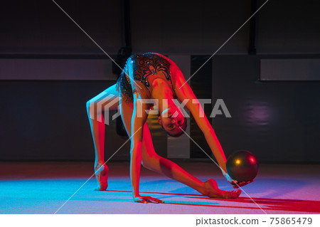 Young graceful girl rhythmic gymnast isolated on dark background in neon light 75865479