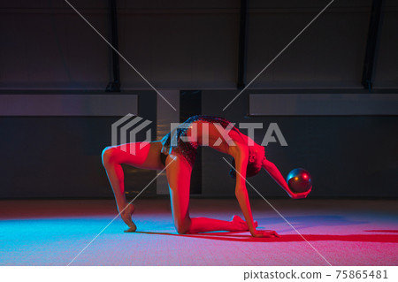 Young graceful girl rhythmic gymnast isolated on dark background in neon light Young graceful girl rhythmic gymnast isolated on dark background in neon light 75865481
