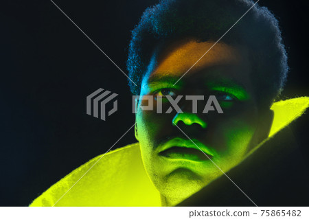 Close up African-American man in yellow glow on dark background in neon light. Close up African-American man in yellow glow on dark background in neon light. 75865482