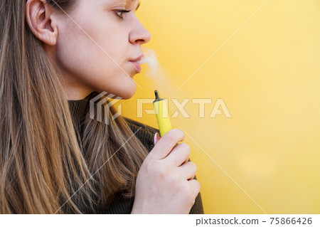 A young girl smokes disposable electronic cigarette. Bright yellow background 75866426