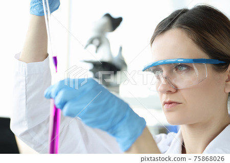 Woman chemist in protective glasses dripping pink liquid into test tube 75868026