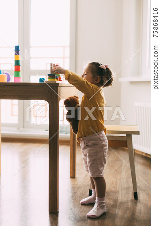 A little girl sorts colorful geometric shapes. Development of motor skills. Development of motor skills and styling of figures. A little girl sorts colorful geometric shapes. Development of motor skills. Development of motor skills and styling of figures. 75868416