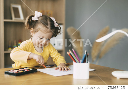 A little girl draws at the table with colored pencils at home or in kindergarten. Childhood, creativity, education. 75868425