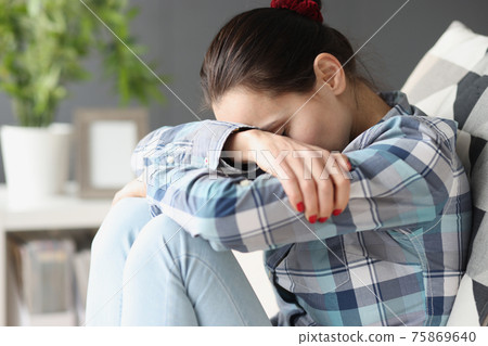 Sad woman sitting with her head bowed on sofa Sad woman sitting with her head bowed on sofa 75869640