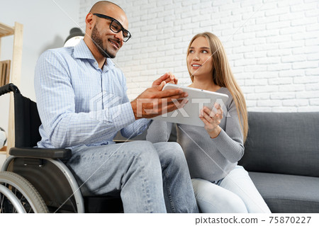 Disabled african american man in wheelchair and his pregnant caucasian wife watch something on digital tablet 75870227