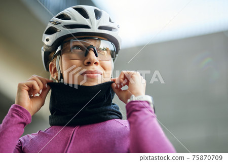 Portrait of professional female cyclist wearing pink suit and neck warmer smiling away while getting ready for training, standing outdoors on a daytime 75870709