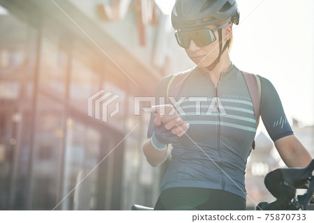 Female cyclist in protective gear using smartphone while riding bicycle in city center. Sportswoman training, exercising outdoors Female cyclist in protective gear using smartphone while riding bicycle in city center. Sportswoman training, exercising outdoors 75870733