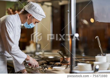 Gentleman in chef uniform switching on the gas stove Gentleman in chef uniform switching on the gas stove 75871080
