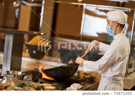 Focused kitchen staff wearing mask and cooking in the wok Focused kitchen staff wearing mask and cooking in the wok 75871103