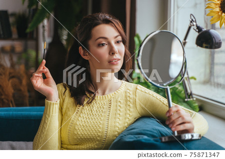 Young pretty woman does makeup at home while looking in the mirror Young pretty woman does makeup at home while looking in the mirror 75871347