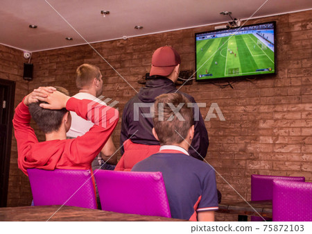 A company of young people indoors playing video games and looking at the screen 75872103