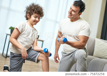Family workout. Sportive latin middle aged father teaching his son exercising with dumbbells while spending time together at home 75872258