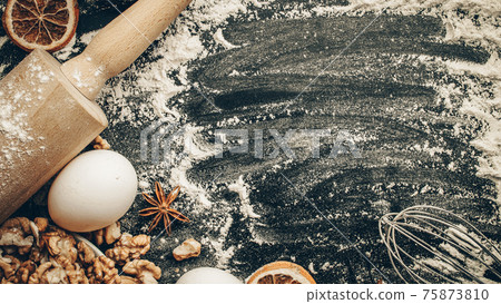 Baker bread. Fresh food ingredients: flour, eggs, nut and star anise, orange on black chalkboard background for bread. Free space for text. Top view. 75873810