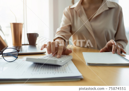 Close up hand of woman using computer calculating household finances or taxes on machine, female manage home family expenditures, using calculator, make payment on laptop Close up hand of woman using computer calculating household finances or taxes on machine, female manage home family expenditures, using calculator, make payment on laptop 75874551
