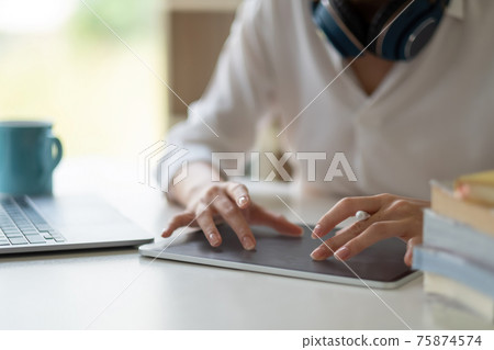 Close up of female worker working from home with digital tablet, laptop and headphone in home office room. Close up of female worker working from home with digital tablet, laptop and headphone in home office room. 75874574