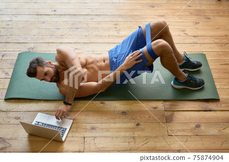 Handsome shirtless man using laptop and working out at home 75874904