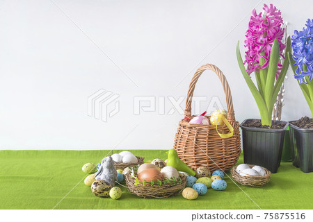 Easter holiday greeting card. Easter eggs in wicker basket, birdnest with eggs and blooming hyacinths in pots; Space for text 75875516