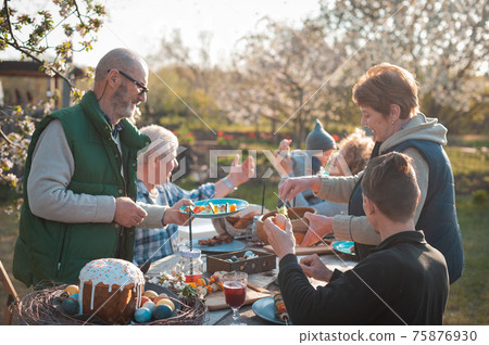 The family gathered at a festive table in the garden to celebrate Easter The family gathered at a festive table in the garden to celebrate Easter 75876930
